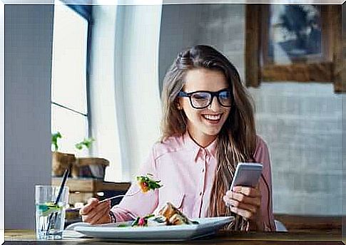 A woman eats while distracted by her phone