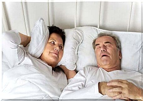 A man snores in bed and his wife holds a pillow to her ears